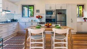 A modern kitchen with white cabinets, a wooden dining table, and a patterned rug. - A Peaceful Haven Only A Few Minutes Walk To Town (KATOOMBA)