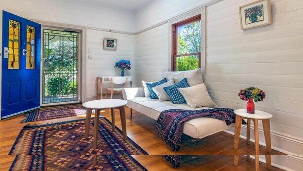A room with a white sofa, a small table, a blue door, and a window with a view of greenery. - A Peaceful Haven Only A Few Minutes Walk To Town (KATOOMBA)