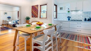 A modern kitchen with white cabinets, a wooden dining table with chairs, and a colorful rug. - A Peaceful Haven Only A Few Minutes Walk To Town (KATOOMBA)