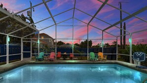 Une piscine extérieure couverte, avec vue sur le coucher du soleil, entourée de chaises et d’un panier de basketball.