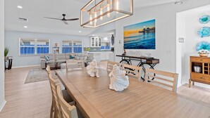 Une cuisine moderne avec un coin repas, un ventilateur de plafond et un tableau représentant un coucher de soleil sur l’eau.