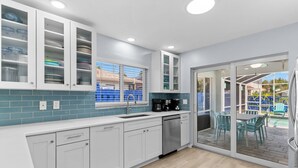 Une cuisine moderne avec des meubles blancs, un lave-vaisselle et une vue sur un patio aménagé avec du mobilier d’extérieur.