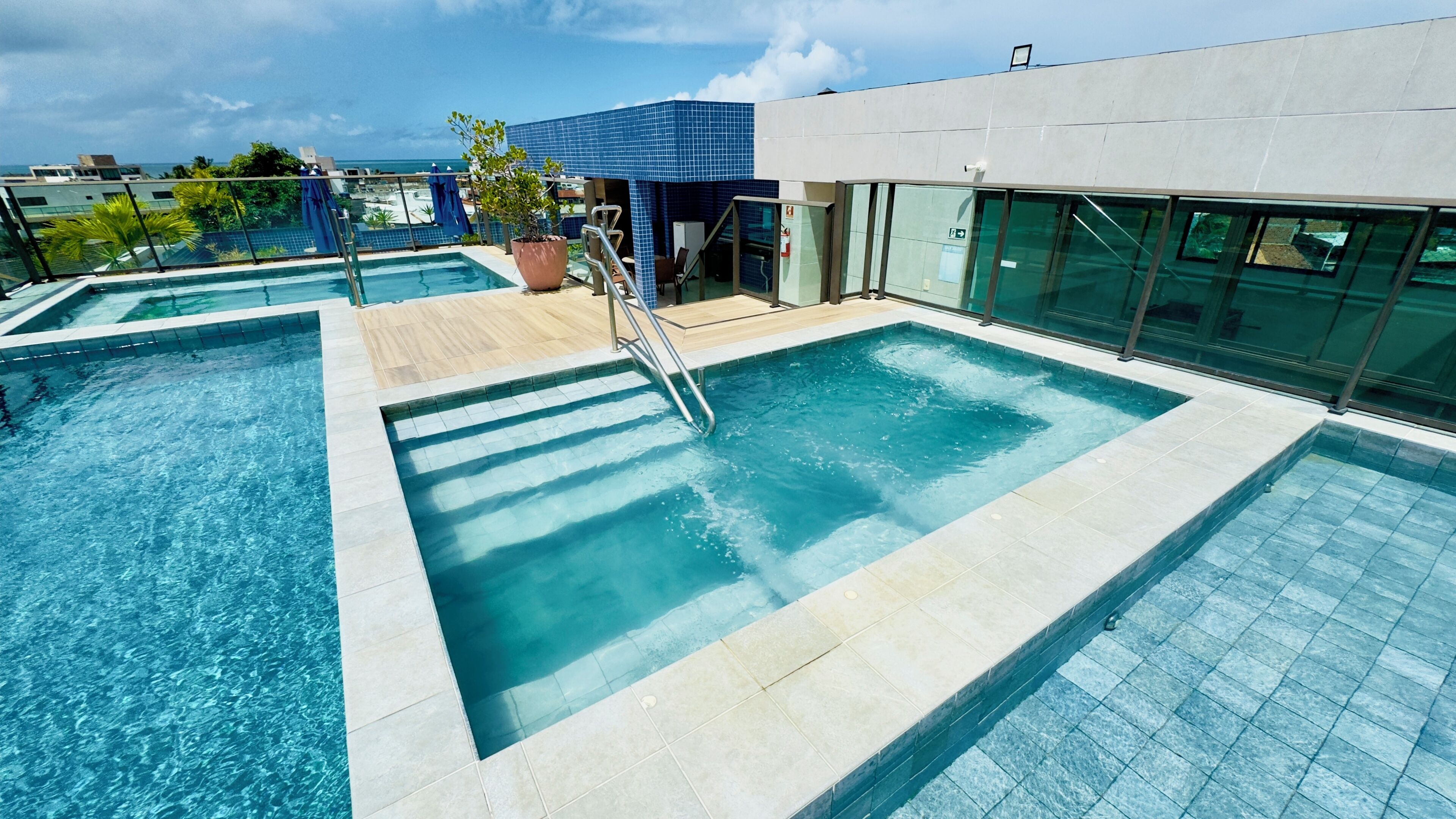 A rooftop pool with clear blue water, a wooden deck, and a view of the ocean.