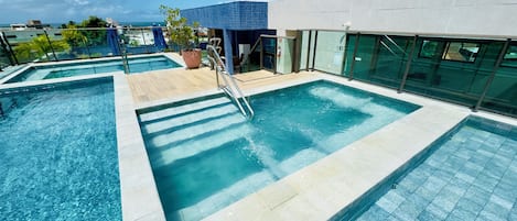 A rooftop pool with clear blue water, a wooden deck, and a view of the ocean.