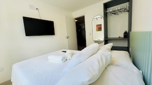 Ein Hotelzimmer mit Bett, Flachbildfernseher an der Wand, Spiegel und einer Tür zu einem Badezimmer.