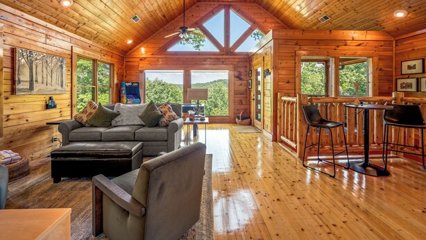 A log cabin interior with a loft bedroom, a dining area, and a living room with a fireplace. - Little Bear: 3-bedroom cabin with Hot Tub, Putt Putt, Game Room & Fire Pit (Sevierville)