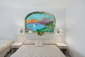 Une chambre à coucher comprenant un lit, deux tables de chevet, une commode, une lampe fixée au mur et un tableau représentant un coucher de soleil sur la mer.