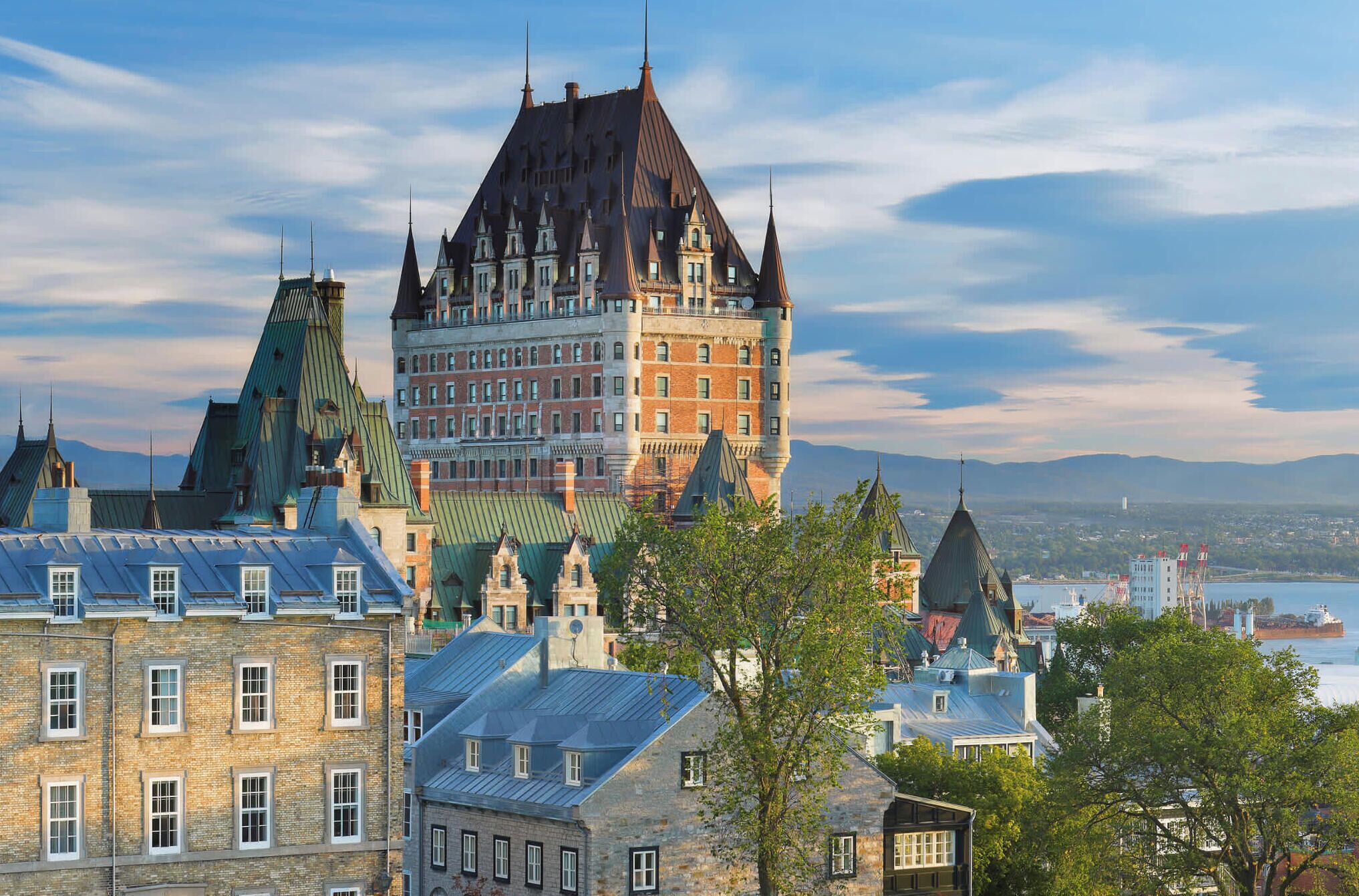 A historic building with multiple towers and a prominent central tower, surrounded by other buildings and a body of water.