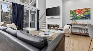 A modern living room with a fireplace, leather sofa, and a TV mounted on the wall. - Private Sunken Spa & Sunroom - Luxury Chalet (Pont-Rouge)