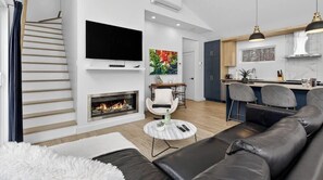 Ein modernes Wohnzimmer mit Kamin, Wand-Fernseher, einer Couch und einem Essbereich mit Bar.