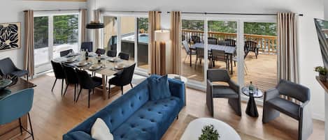 A spacious living area with a blue sofa, dining table set, and a view of a deck with outdoor seating.