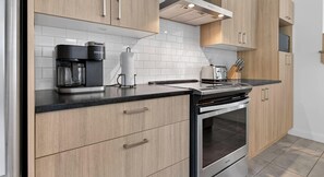 Una cocina moderna con armarios de madera, encimera negra, cafetera, tostadora y horno.
