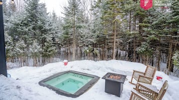 Ein verschneiter Außenbereich mit Whirlpool, Feuerstelle und Korbstühlen.