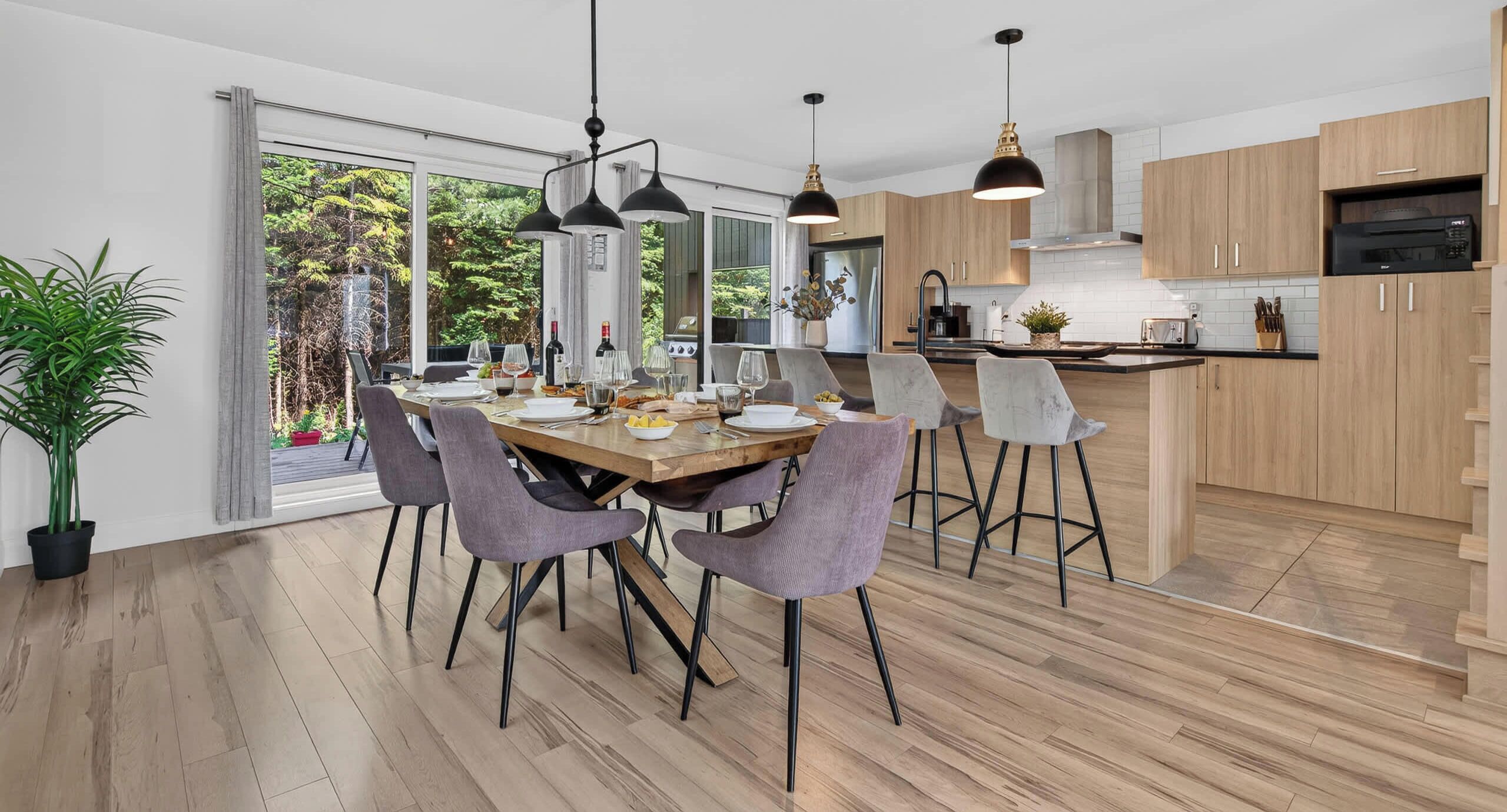 Una cocina moderna con armarios de madera, una zona de comedor con una mesa y sillas de madera, y un ventanal con vistas a zonas verdes.