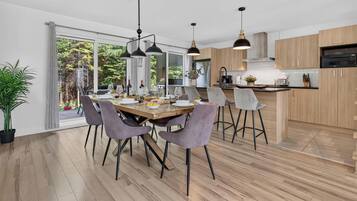 Una cocina moderna con armarios de madera, una zona de comedor con una mesa y sillas de madera, y un ventanal con vistas a zonas verdes.