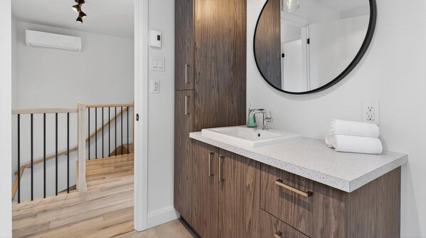 Un baño moderno con tocador de madera, un espejo grande, un lavabo y un perchero para toallas.