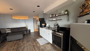 A modern kitchen with white cabinets, a black stove, and a microwave. There is a grey sofa and a small table with a plant. - Lake View Terrace with Pool (Osoyoos)