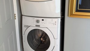 A stacked washer and dryer unit in a hallway with a framed picture on the wall. - Lake View Terrace with Pool (Osoyoos)