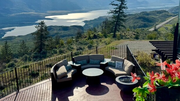 A deck with a curved sofa and a round table, overlooking a lake and mountains. - Lake View Terrace with Pool (Osoyoos)