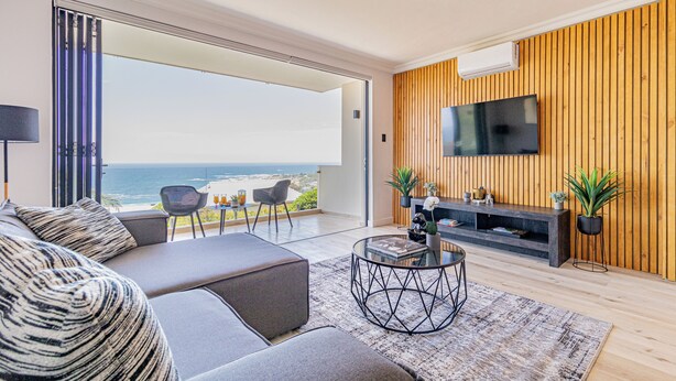 A modern living room with a sofa, a coffee table, and a TV mounted on a wooden wall. - Stunning 2-bedroom apartment in gorgeous Camps Bay - 5 mins from the beach. (Cape Town)
