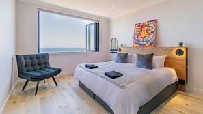 A bedroom with a large window, a bed with pillows, a chair, and a painting on the wall. - Stunning 2-bedroom apartment in gorgeous Camps Bay - 5 mins from the beach. (Cape Town)