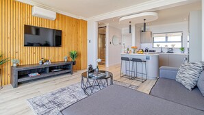 A modern living room with a TV, sofa, coffee table, and a kitchen area with bar stools. - Stunning 2-bedroom apartment in gorgeous Camps Bay - 5 mins from the beach. (Cape Town)