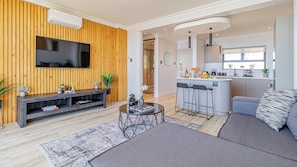 A modern living room with a TV, sofa, coffee table, and a kitchen area with bar stools. - Stunning 2-bedroom apartment in gorgeous Camps Bay - 5 mins from the beach. (Cape Town)