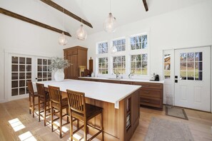 A spacious kitchen with a large island, wooden chairs, and pendant lights. - Historic Bones, Entirely New Soul | Designer Lux (Sandwich)