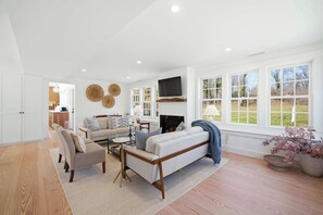A spacious living room with a sofa, armchair, and coffee table, a fireplace, and large windows. - Historic Bones, Entirely New Soul | Designer Lux (Sandwich)