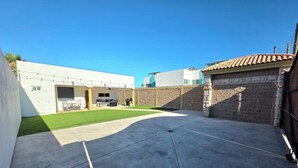 A residential backyard with a paved area, a lawn, and a stone wall.