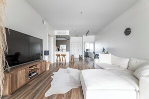 Ein modernes Wohnzimmer mit einem großen Flachbildfernseher, einem weißen Sofa, einer Holz-Unterhaltungseinrichtung und einem Kuhfellteppich.