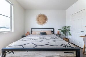 Un dormitorio con una cama, un adorno de sol en la pared, una planta en maceta y vistas a través de una ventana.