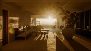 A spacious living area with a large sofa, a coffee table, and a view of the ocean at sunset. - Zima Stays (Acapulco)
