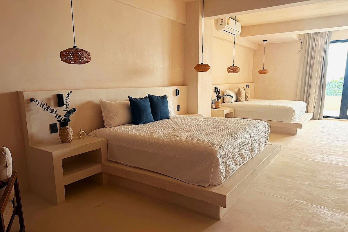 A modern bedroom with a large bed, bedside tables, and hanging lights.