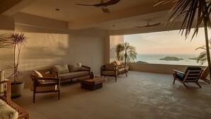 A spacious living area with a sofa, chairs, a coffee table, ceiling fans, and a view of the ocean.