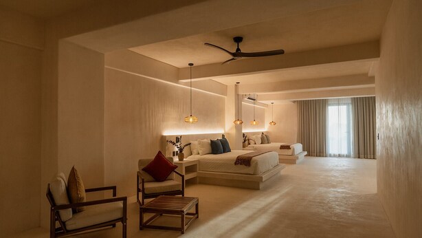 A spacious hotel room with a large bed, a sitting area with a chair and a small table, a ceiling fan, and a view of the outside through a large window. - Zima Stays (Acapulco)