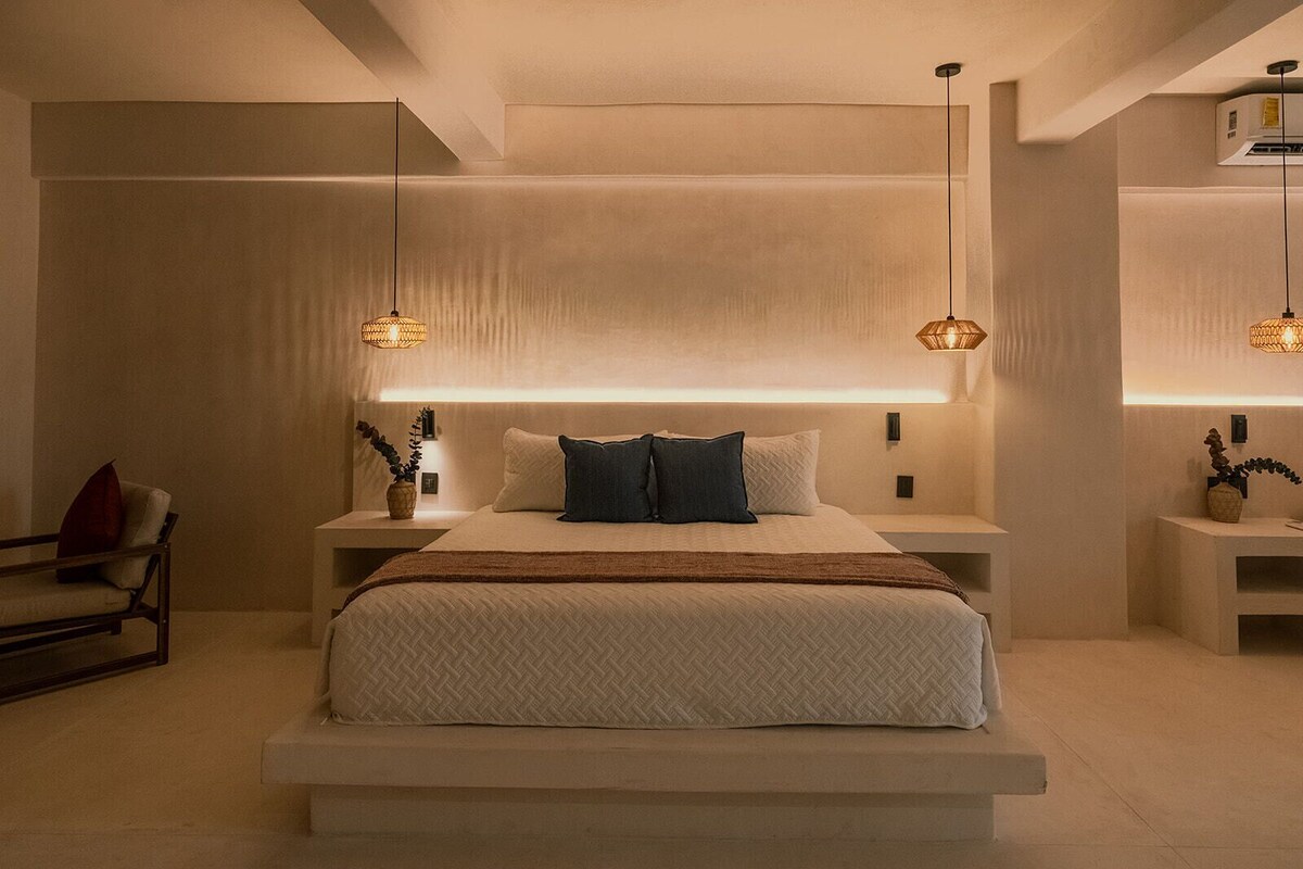 A modern bedroom with a large bed, bedside tables, and pendant lights.
