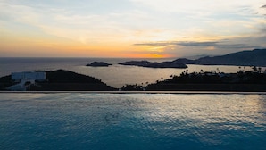 A coastal view with a swimming pool, distant islands, and a sunset.