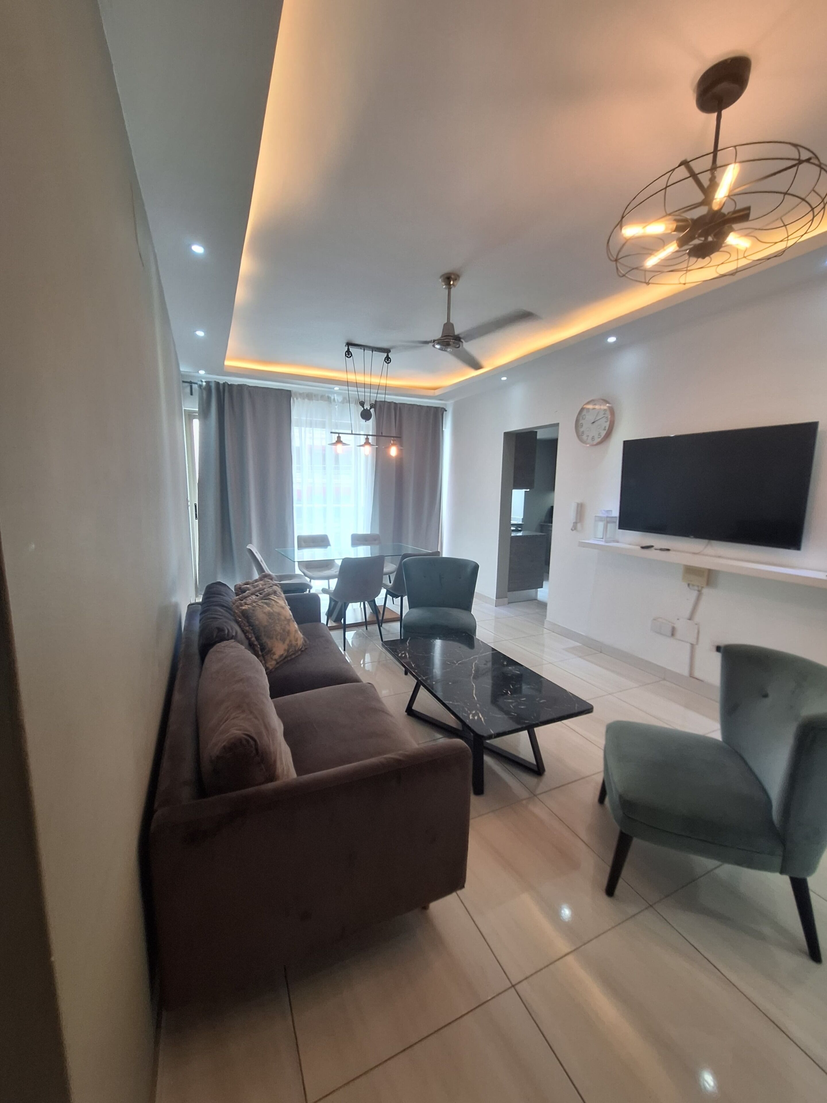 Una sala de estar moderna con un sofá, sillas, una mesa de centro, un televisor y un ventilador de techo.