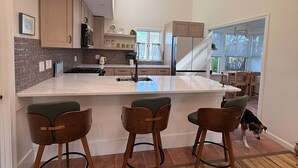 A modern kitchen with a large island, wooden bar stools, and a skylight. - Modern Cape Beach Escape - Classic Coastal Charm (Falmouth)