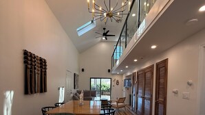 A modern dining area with a marble table, black chairs, a chandelier, and a view of the outdoors. - Modern Cape Beach Escape - Classic Coastal Charm (Falmouth)