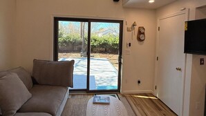 A living room with a sofa, a round coffee table, a sliding glass door leading to an outdoor area, and a staircase. - Modern Cape Beach Escape - Classic Coastal Charm (Falmouth)