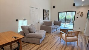 A modern living room with a wooden floor, a sofa, a dining table, and a chair. - Modern Cape Beach Escape - Classic Coastal Charm (Falmouth)