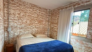 A bedroom with a bed, a window with curtains, a wall with a brick pattern, and a ceiling light. - Cozy chalet in Conceição do Ibitipoca, 800 meters from the town center. (Conceição da Ibitipoca)