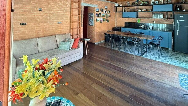 A spacious living area with a wooden ceiling, a brick wall, a sofa, a dining table with chairs, and a kitchen area with a refrigerator and shelves. - Cozy chalet in Conceição do Ibitipoca, 800 meters from the town center. (Conceição da Ibitipoca)