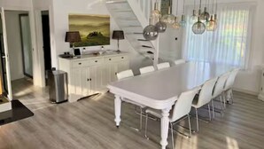 A modern kitchen with a white island, a dining table with chairs, a staircase, and pendant lighting. - Sunny Pool Villa at Vinkeveense Plassen | 20 Min from Amsterdam (Vinkeveen)