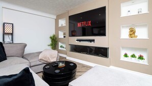 A modern living room with a flat-screen TV, a round coffee table, a sofa, and decorative shelves. - Fife Coast Stay with Parking & Garden in Rosyth - WiFi (Rosyth)