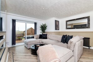A modern living room with a sectional sofa, a coffee table, a large mirror, and a sliding glass door leading to a balcony. - Fife Coast Stay with Parking & Garden in Rosyth - WiFi (Rosyth)