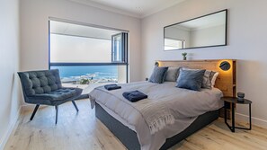 A bedroom with a large bed, a chair, a bedside table, a mirror, and a view of the sea. - Full spec apartment with stunning ocean views in the heart of Camps Bay (Cape Town)