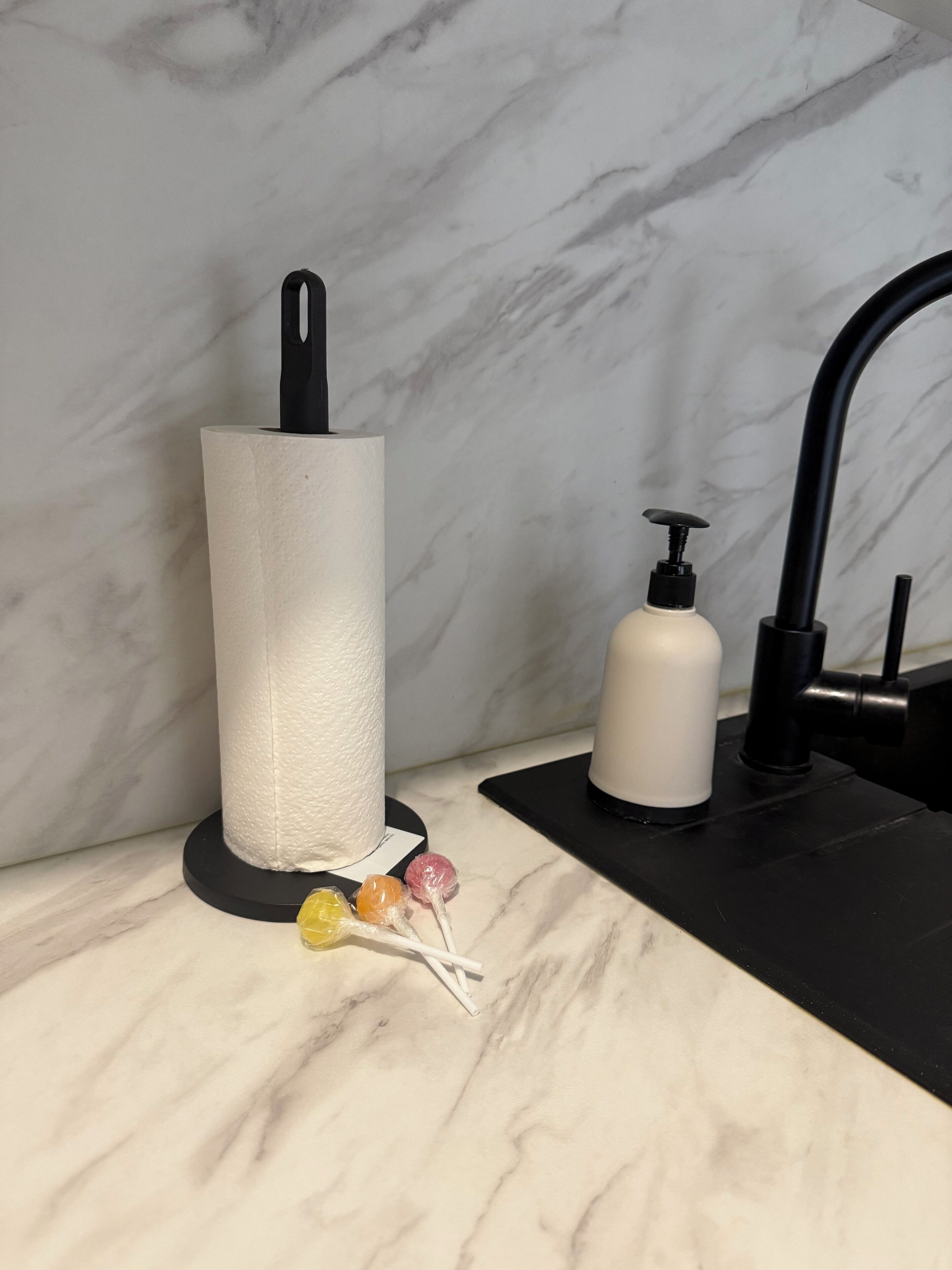 Une salle de bain avec un comptoir en marbre, un porte-serviettes en papier, un distributeur de savon et un robinet.